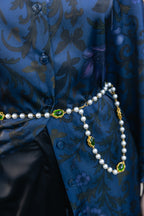 Pearl necklace and pearl belt with green and gold accents on a blue patterned fabric background