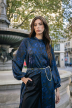 Woman in a blue gloral dress and a pearl belt standing in an urban setting with trees and buildings in Paris.