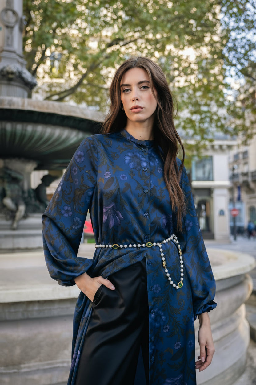 Woman in a blue gloral dress and a pearl belt standing in an urban setting with trees and buildings in Paris.