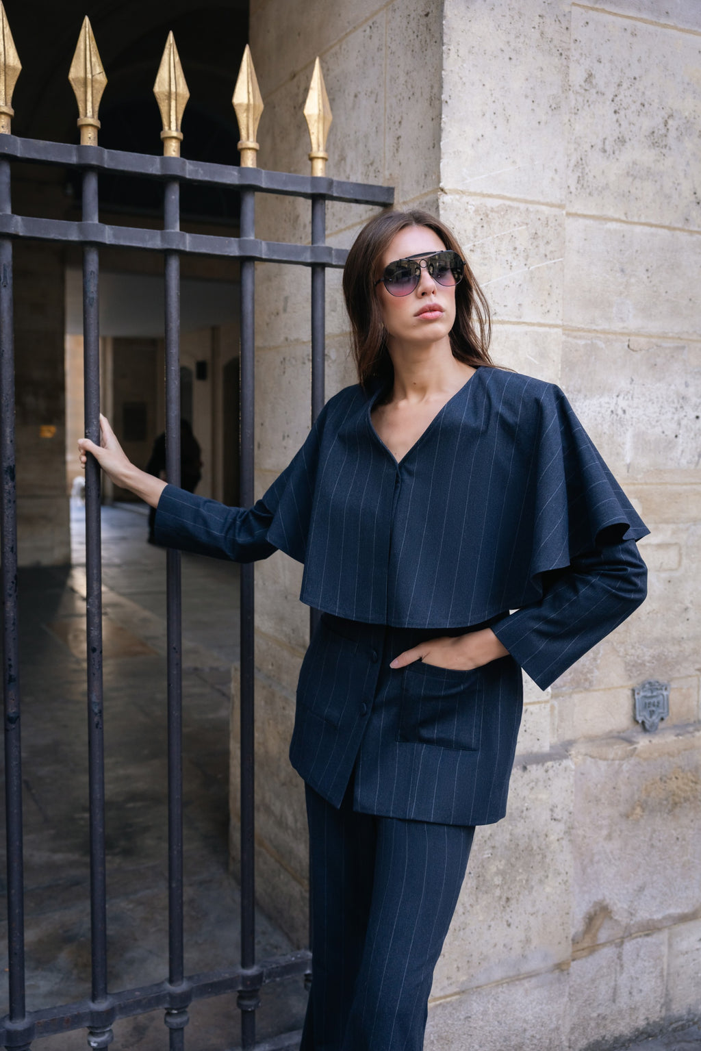 Woman in a navy blue outfit standing against a stone wall.