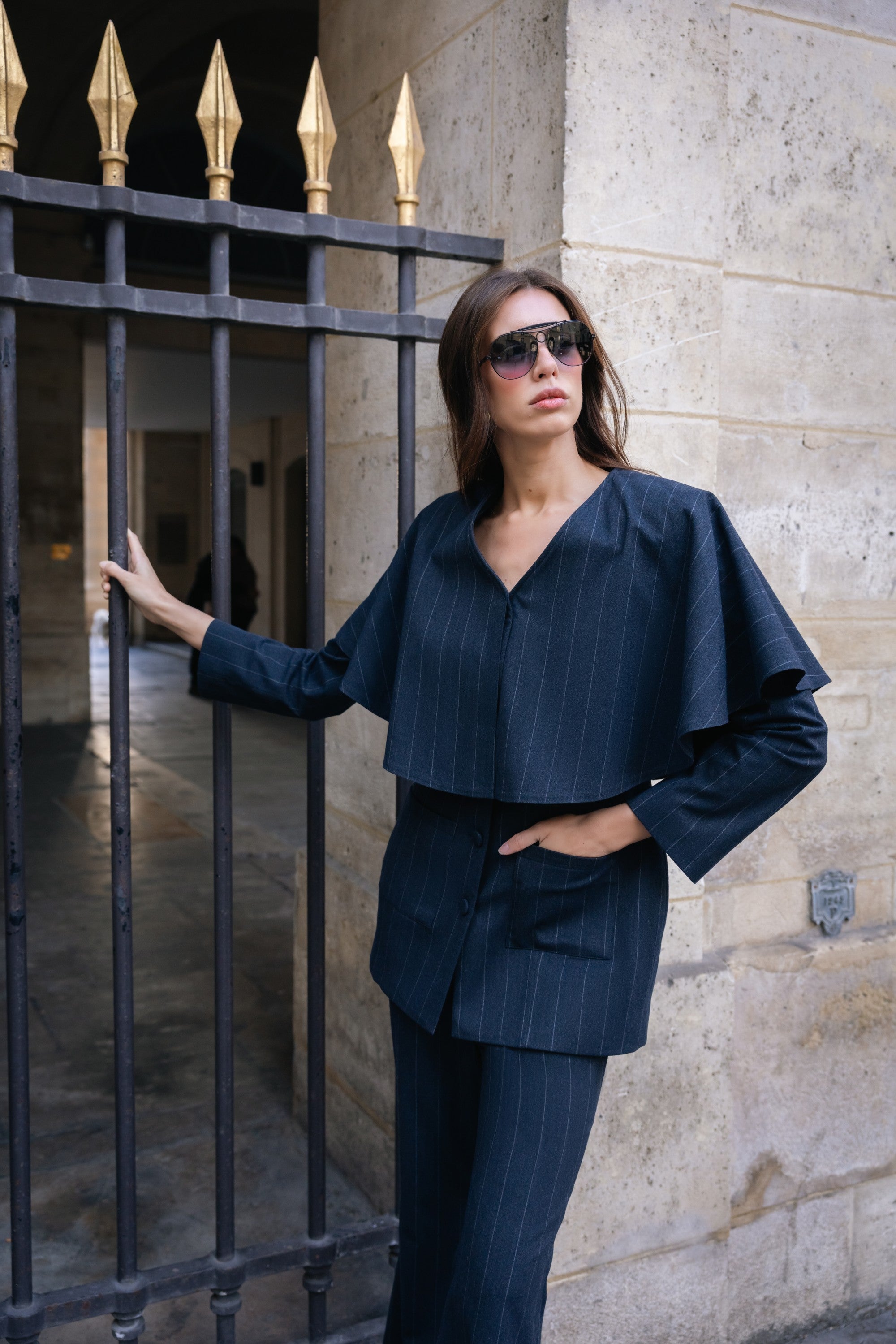Woman in a navy blue outfit standing against a stone wall.