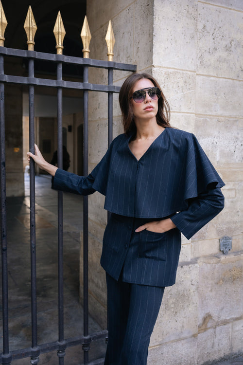 Woman in a navy blue outfit standing against a stone wall.