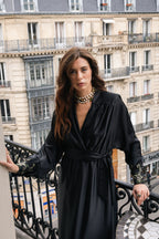 Woman in a black dress standing on a balcony with a Parisian cityscape background. Premium satin. Silk embroidery. Hand embroidery. 
