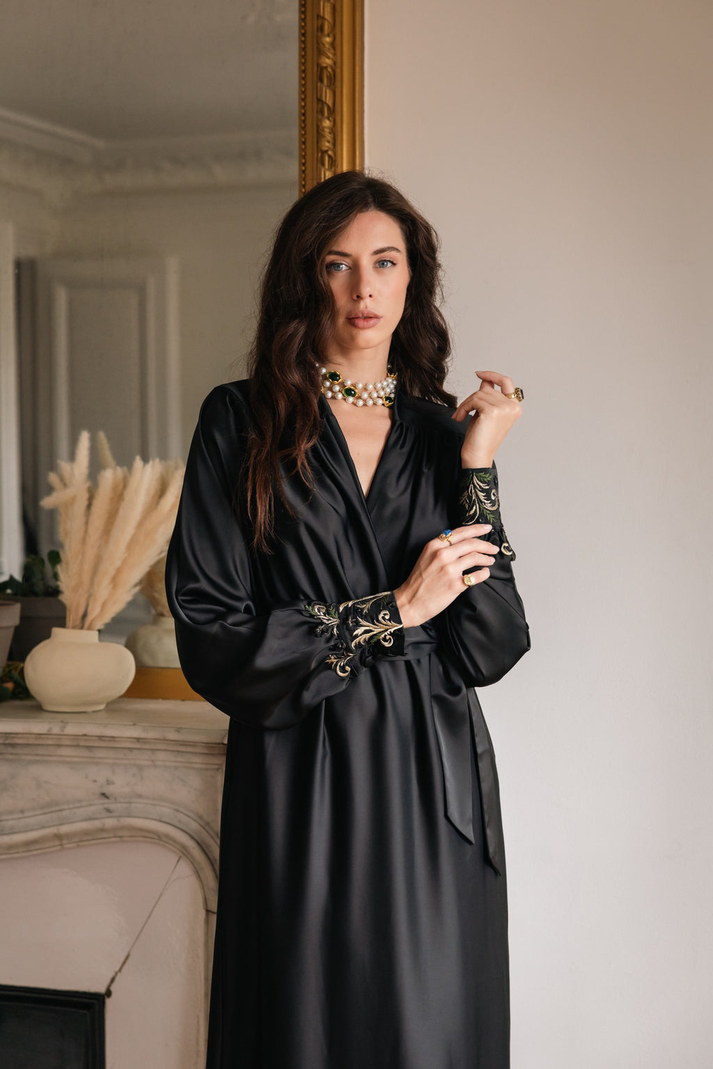 Woman wearing a black dress with gold embroidery in an elegant room.