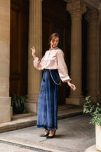 Woman in a pink blouse and blue pants standing in front of classical architecture.