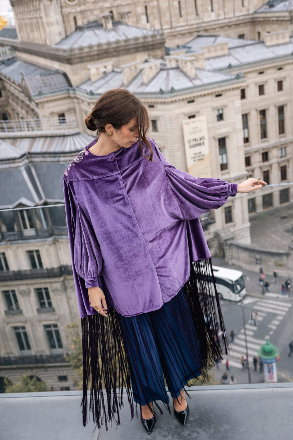 Woman wearing a purple velvet top with fringe sleeves and blue pleated skirt in Paris.
